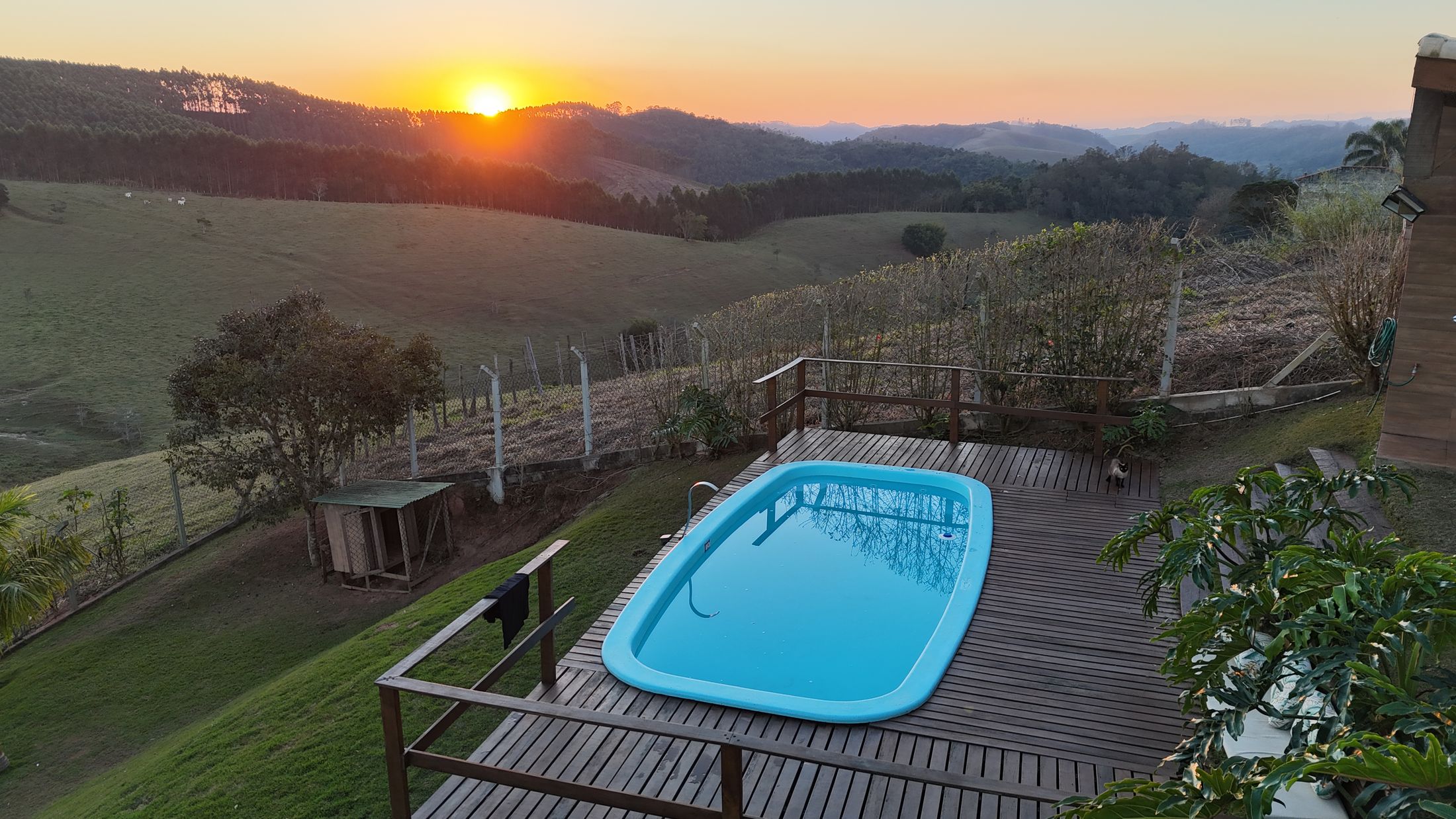 Piscina com deck de madeira e o pôr do sol sobre as colinas de Santa Branca