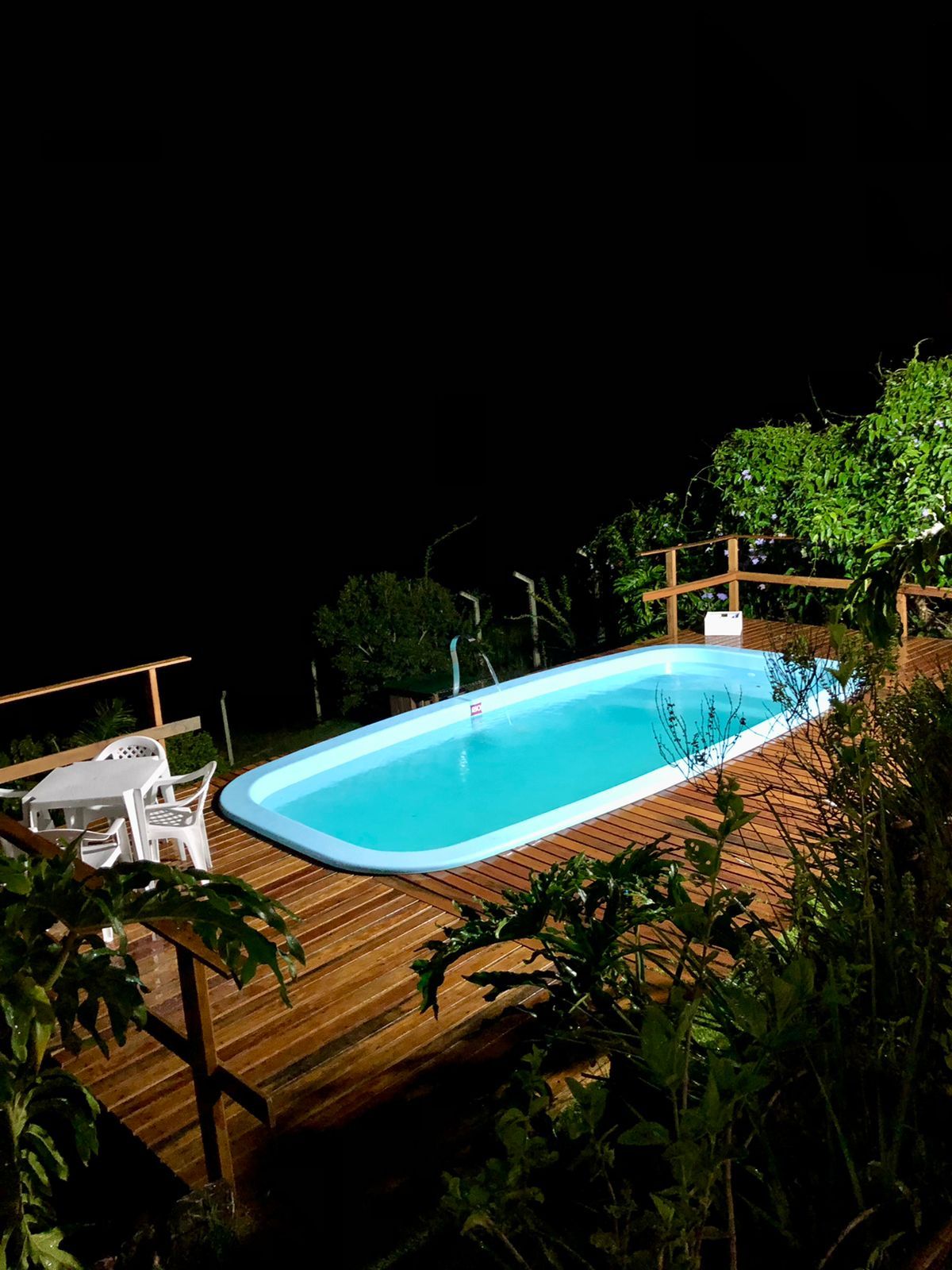 Piscina iluminada à noite com deck de madeira
